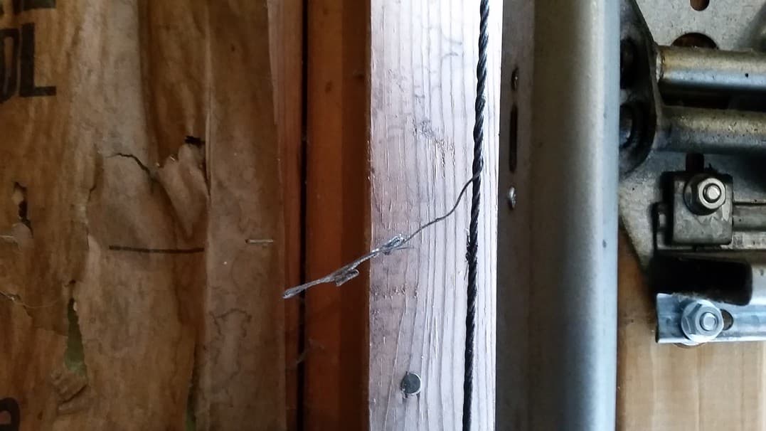 A garage door lift cable beside the track, with frayed strands of wire sticking out