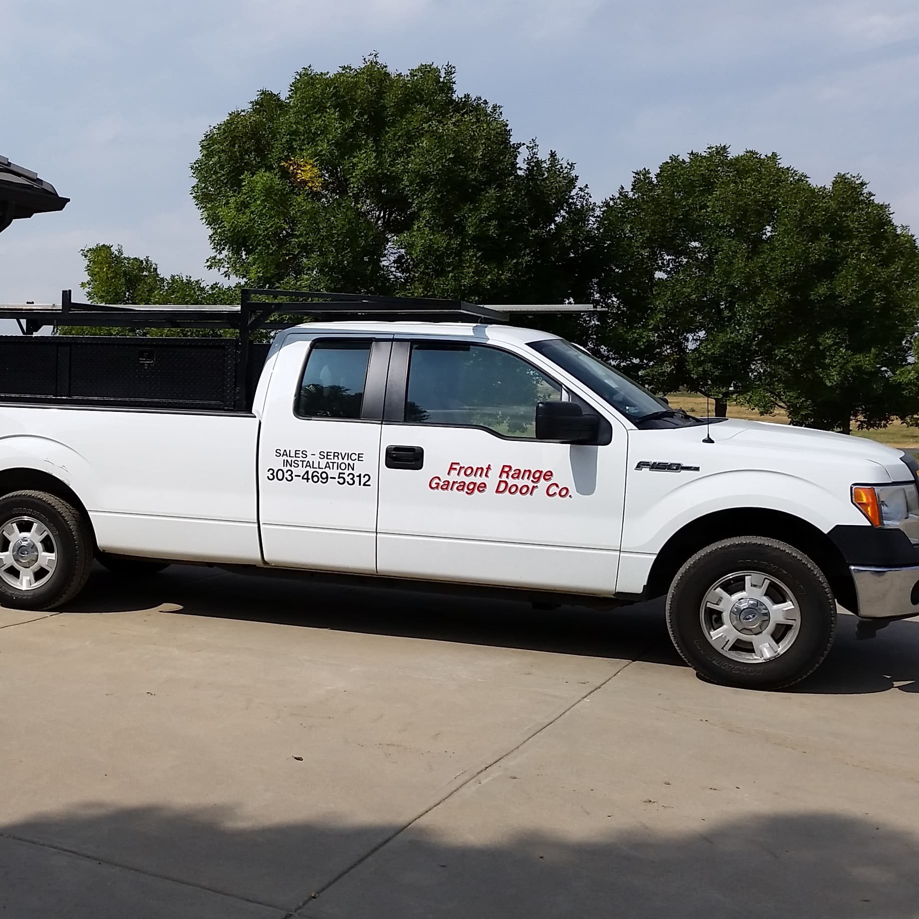 Front Range Garage Door Co. work truck, a white Ford F-150 with a ladder rack, parked on a driveway